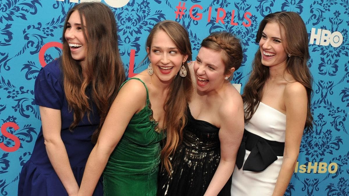 Four female actresses smiling and laughing at something off camera to the left, while standing in a line at a premiere.